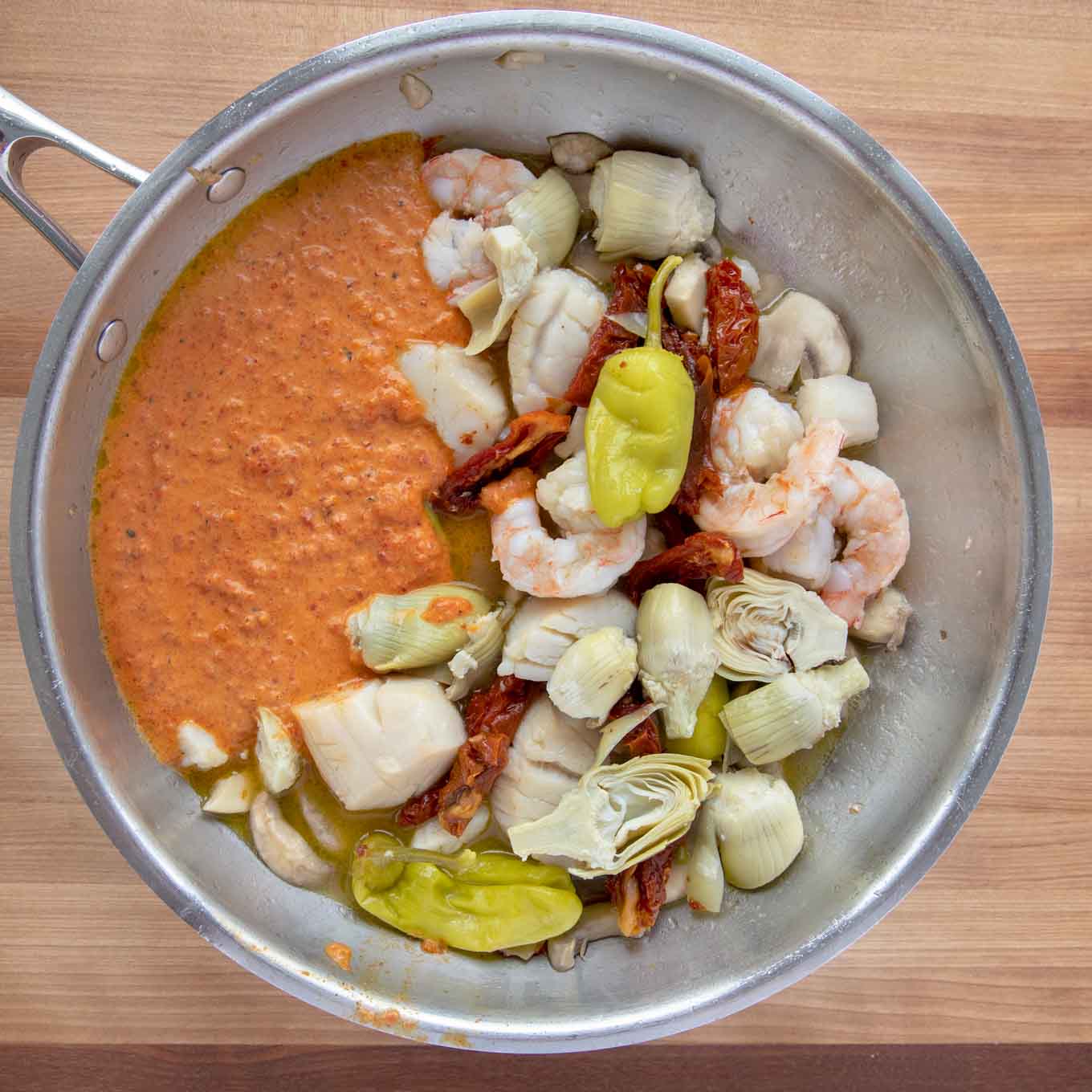 cooked shrimp, scallops and mushrooms in a saute pan with artichokes, sun-dried tomatoes, pepperoncini and roasted red pepper sauce