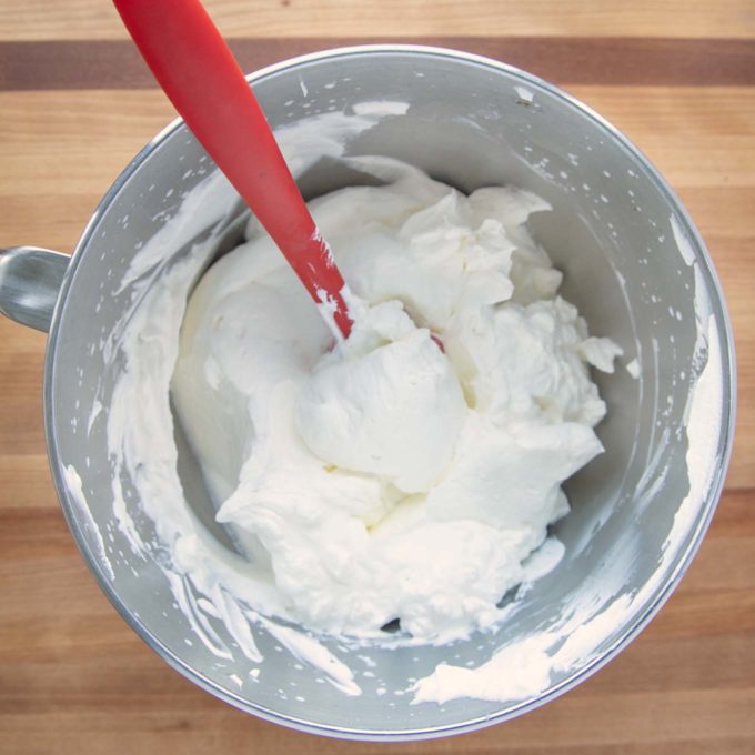whipped cream in a mixer bowl with a red rubber spatula