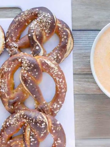 beer pretzels on a white tray with a bowl of cheddar sauce next to it
