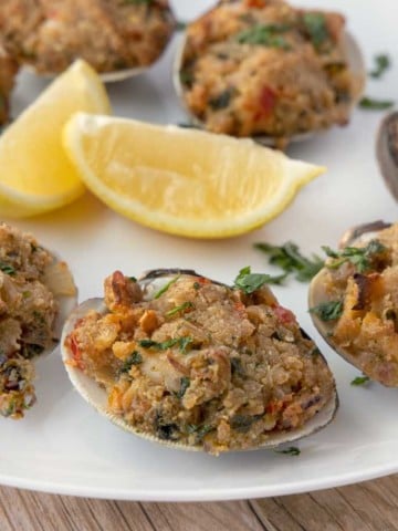 deviled clams on a white plate with lemon wedges