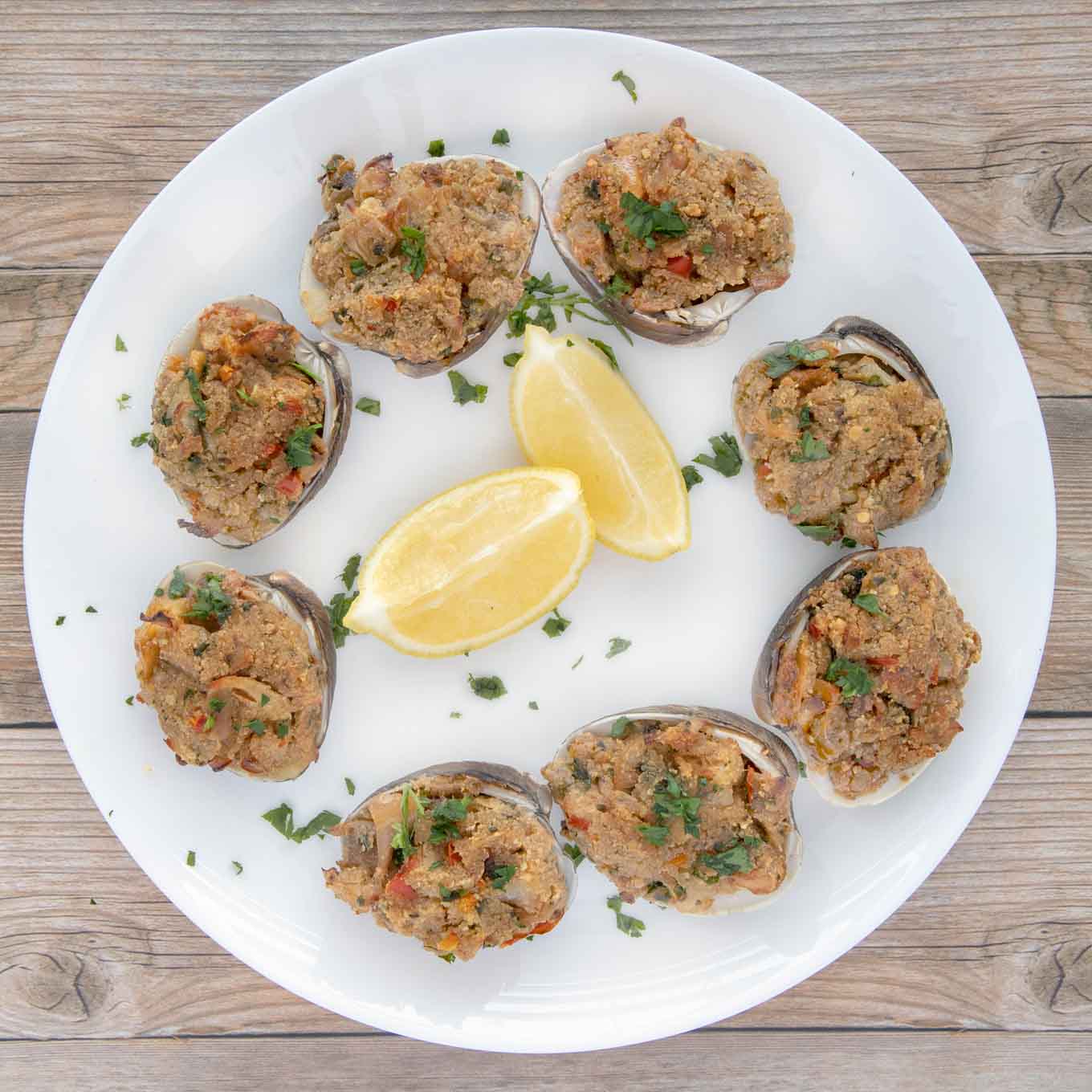 cooked deviled clams on a white plate with lemon wedges