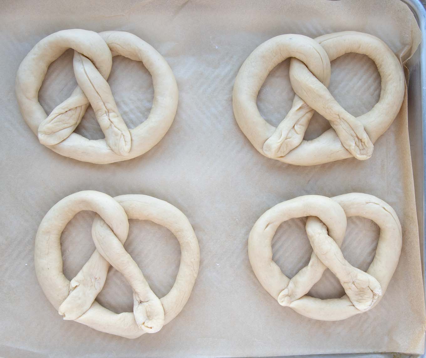 formed raw pretzels on parchment on baking sheet