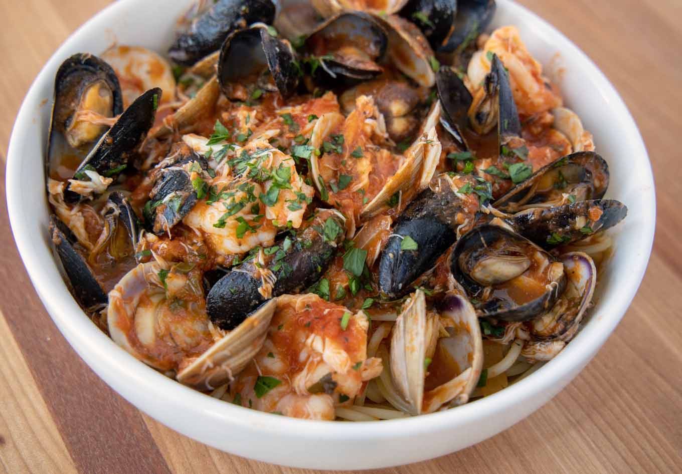 seafood in a marinara sauce served over pasta in a white bowl