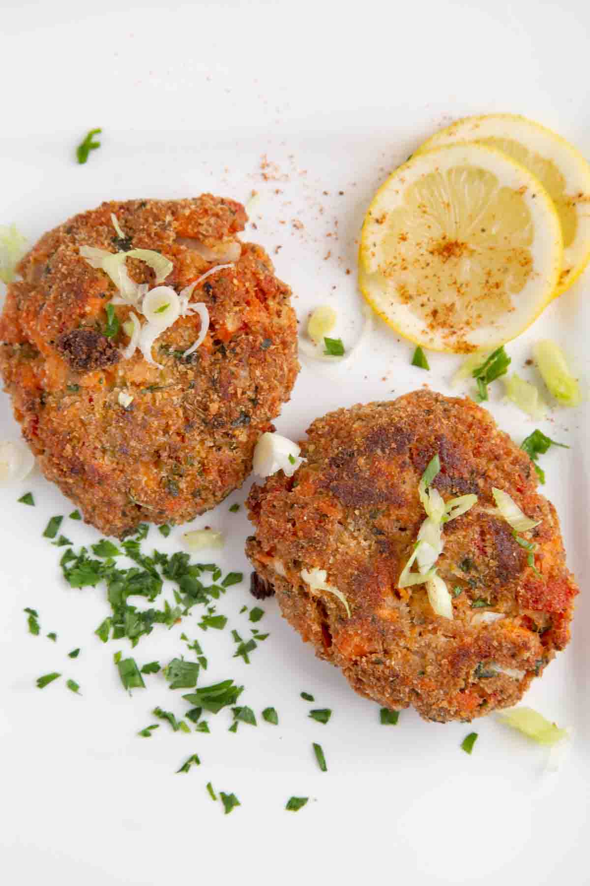 two salmon patties on a white plate with lemon circles