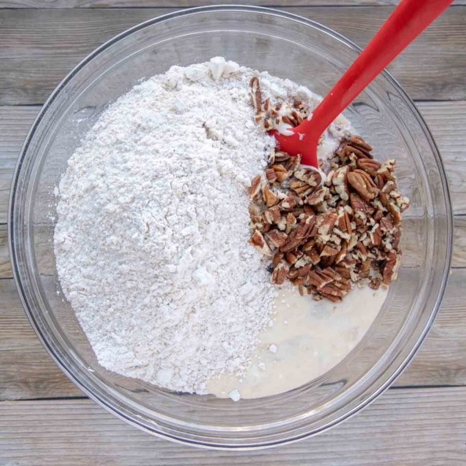 pecans and flour mixture added to the wet ingredients with a red silicone spatula in the bowl
