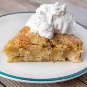 slice of buttery apple cake topped with whipped cream on a white plate