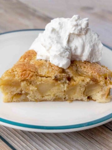 slice of buttery apple cake topped with whipped cream on a white plate