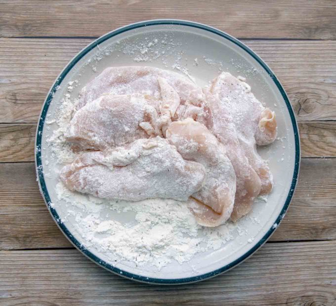 chicken breasts in seasoned flour mixture on a plate