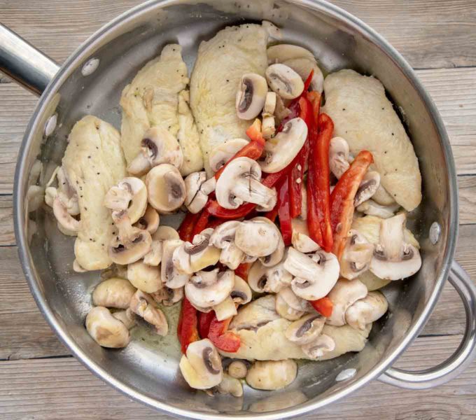 chicken breasts mushrooms and sliced red peppers in a large saute pan