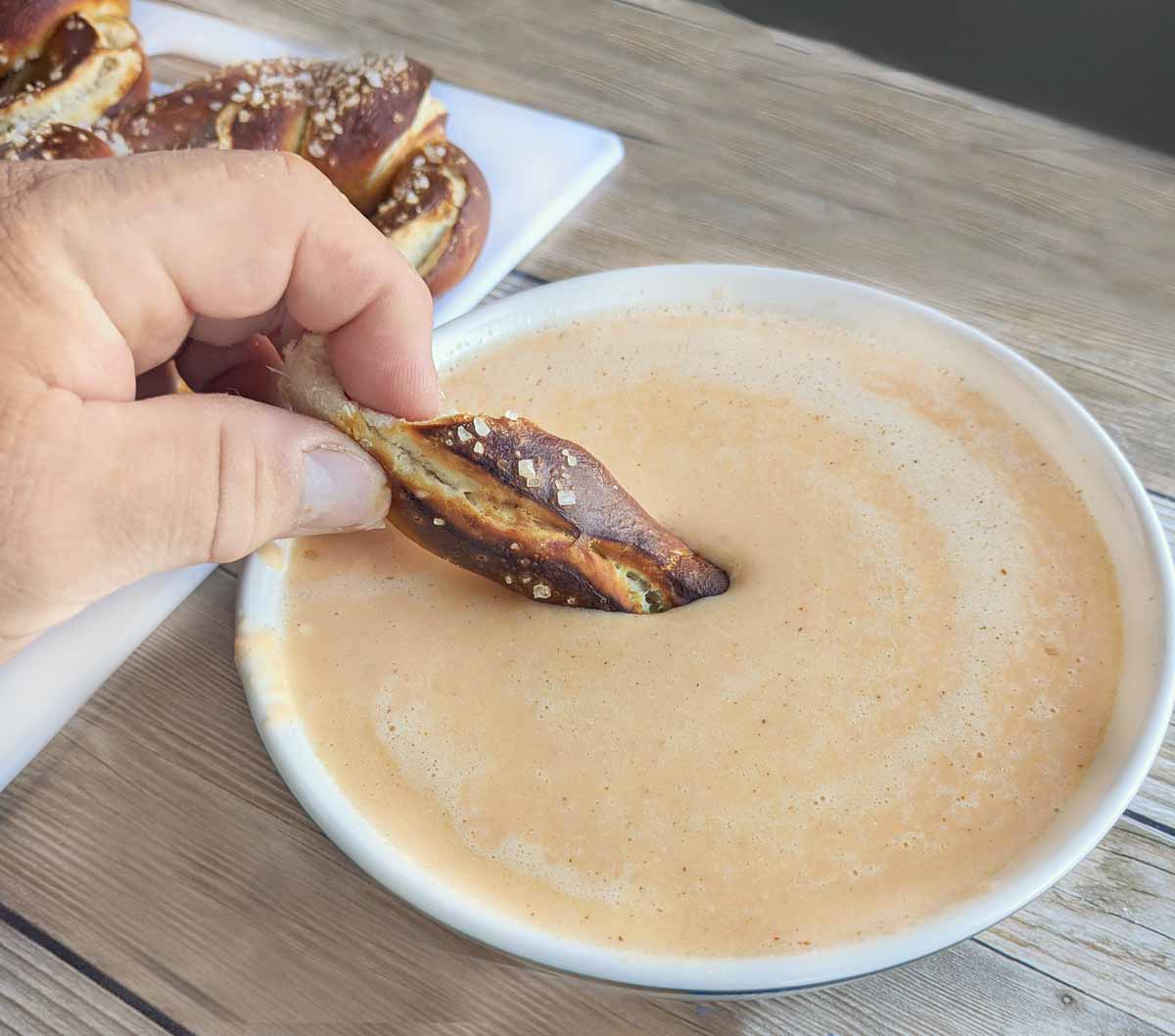 hand dipping part of pretzel in cheese sauce