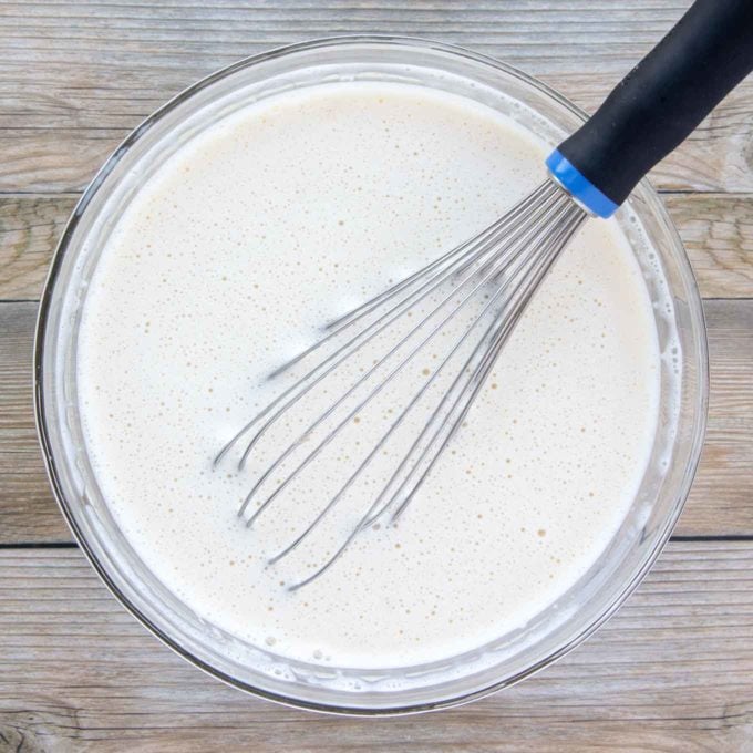 milk and vanilla added to egg mixture in a glass bowl with a wire whisk