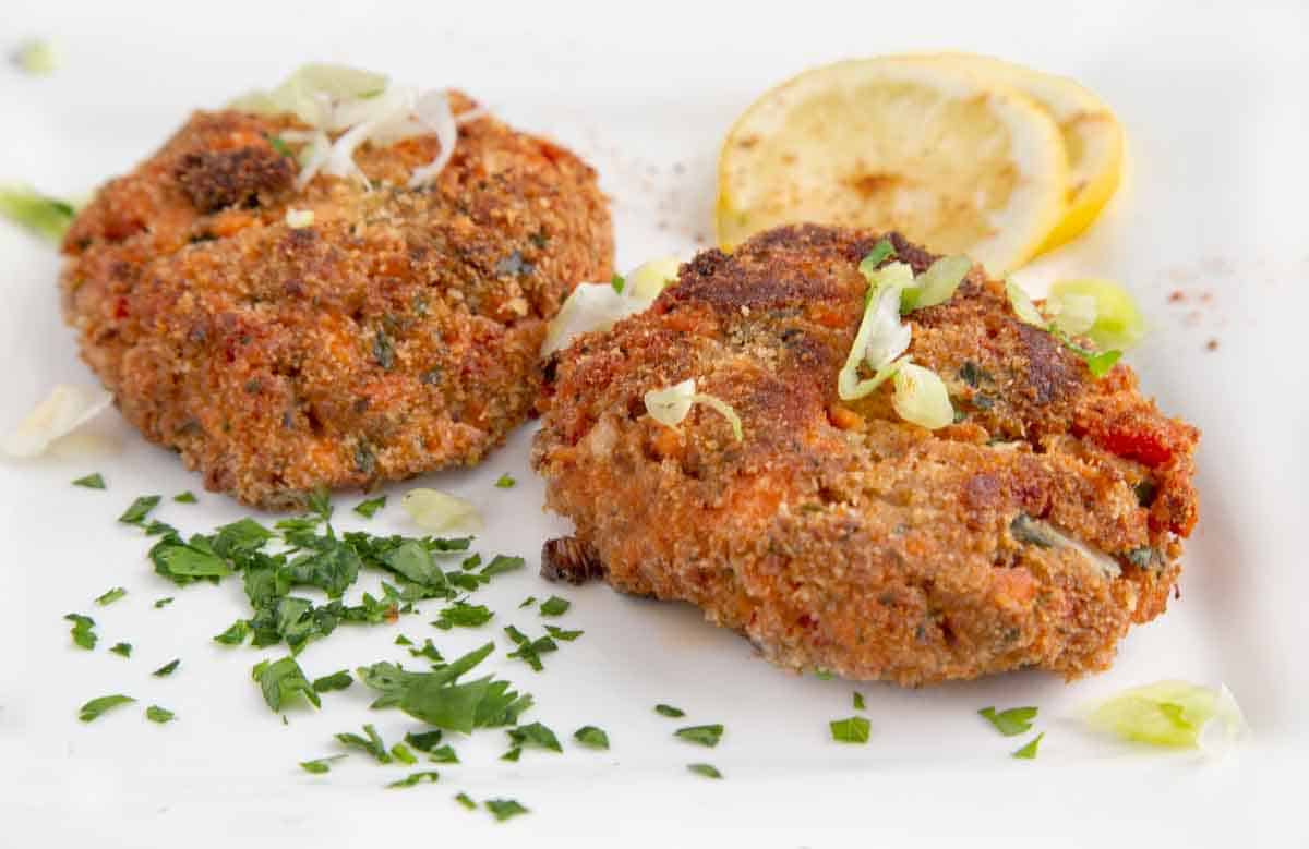two salmon patties on a white plate with lemon circles