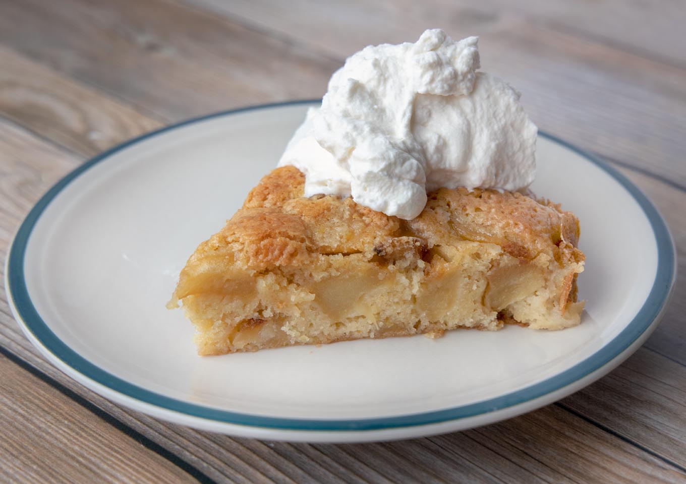 slice of buttery apple cake with whipped cream on a plate