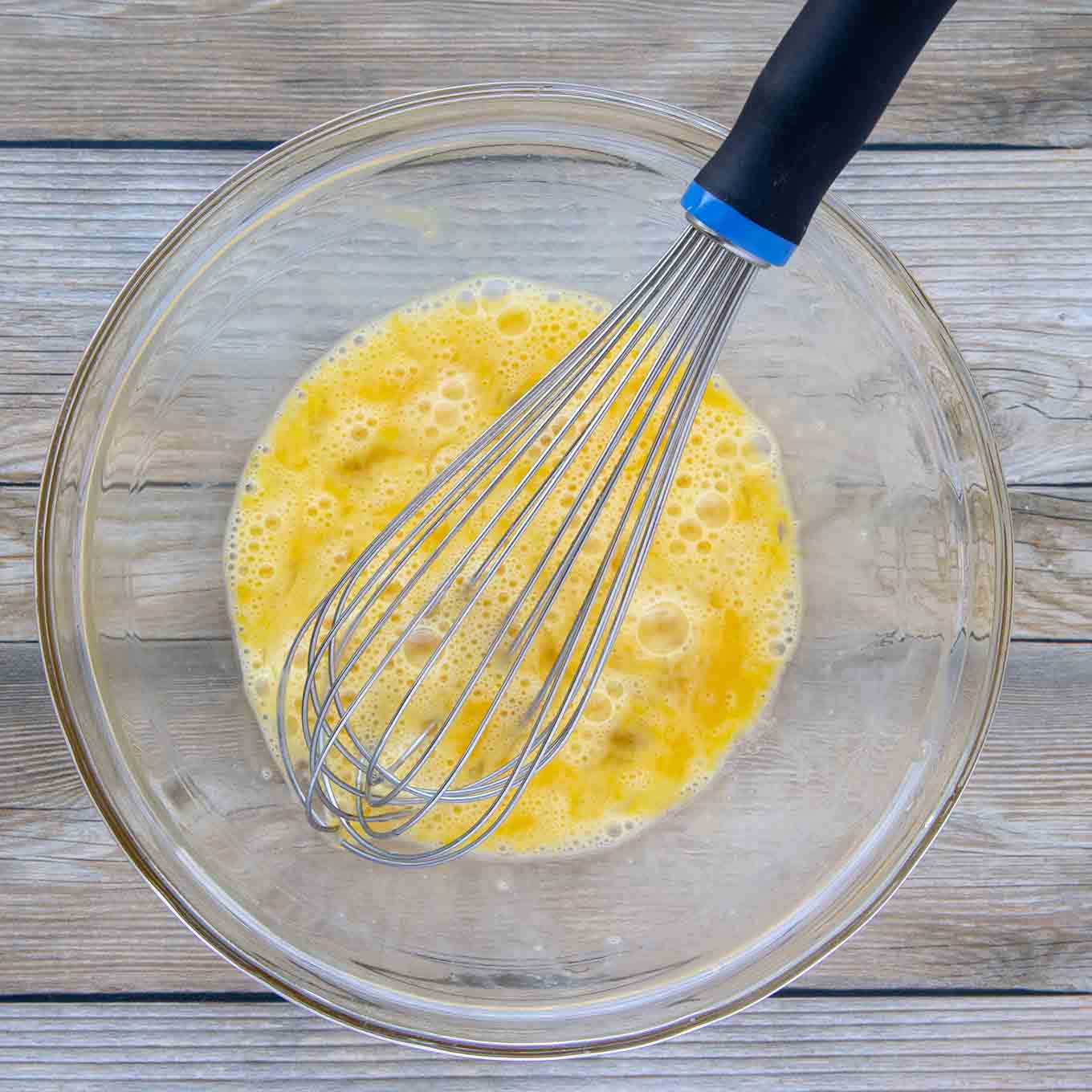 whisked. eggs in a glass bowl with a wire whisk