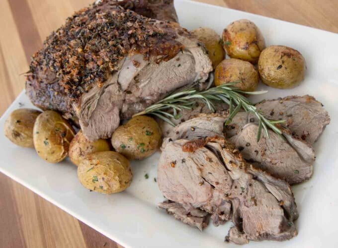 roast leg of lamb and slices with whole baby potatoes on a white platter