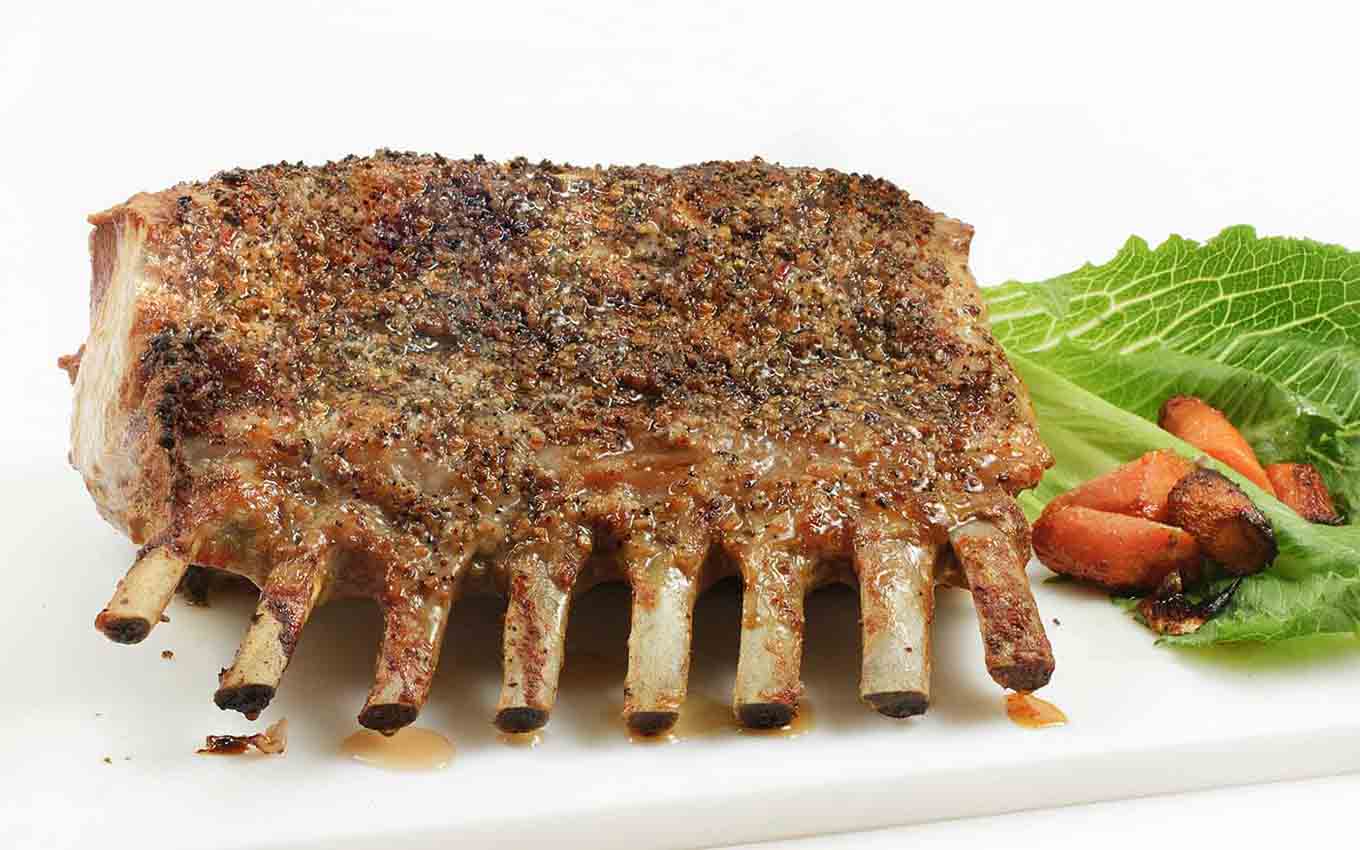 bone in roasted rack of pork on a white cutting board with a  romaine leaf and cooked carrots on the side