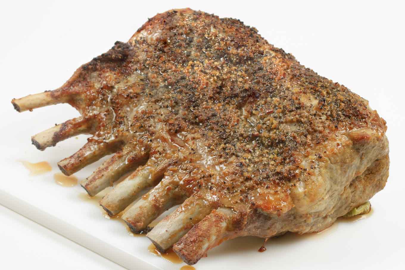 roasted rack of pork with a montreal seasoning crust on a white cutting board