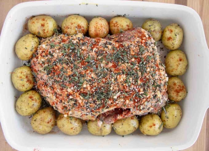 seasoned leg of lamb in a baking pan surrounded by baby potatoes