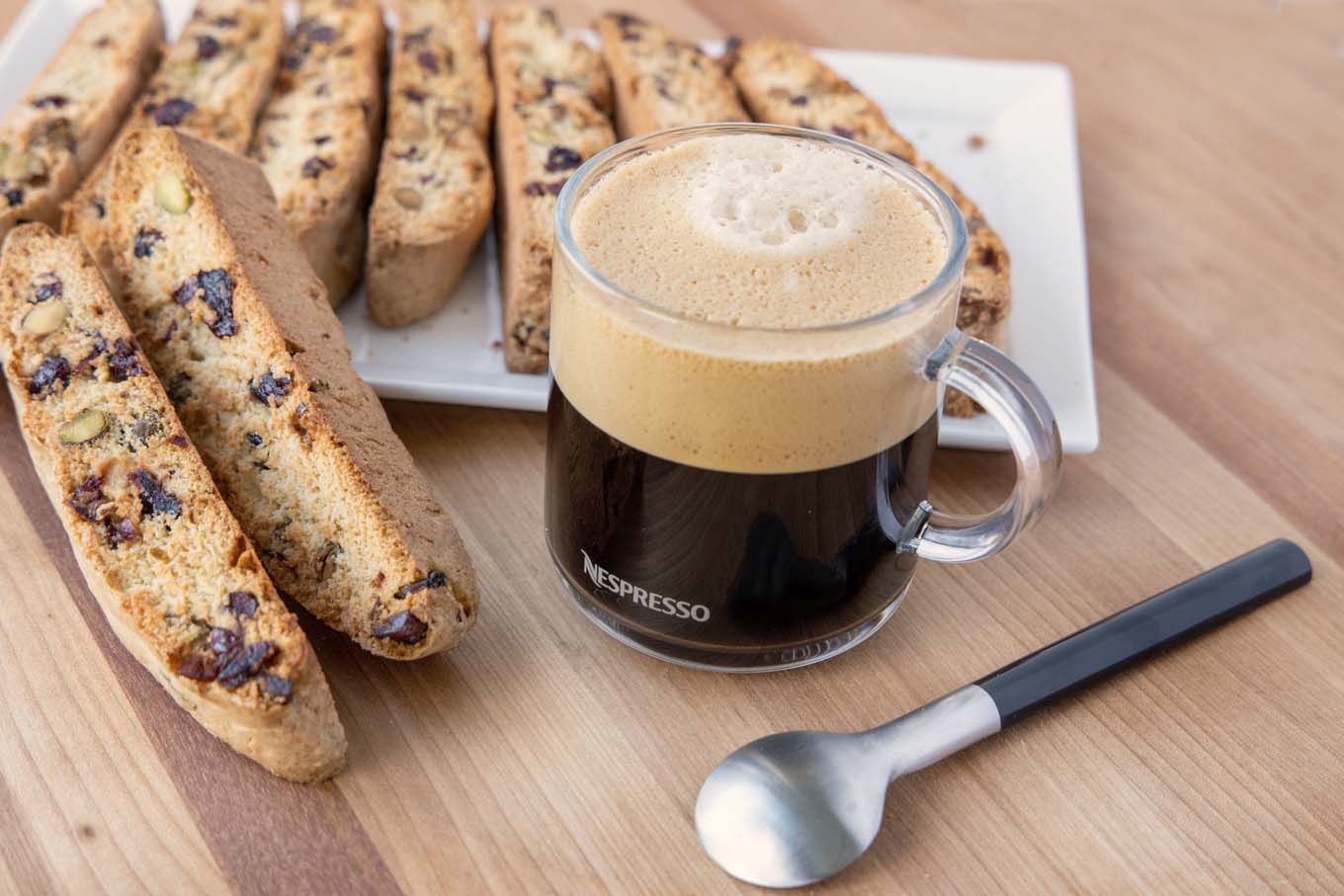 glass cup of coffee with biscotti on a tray and a spoon