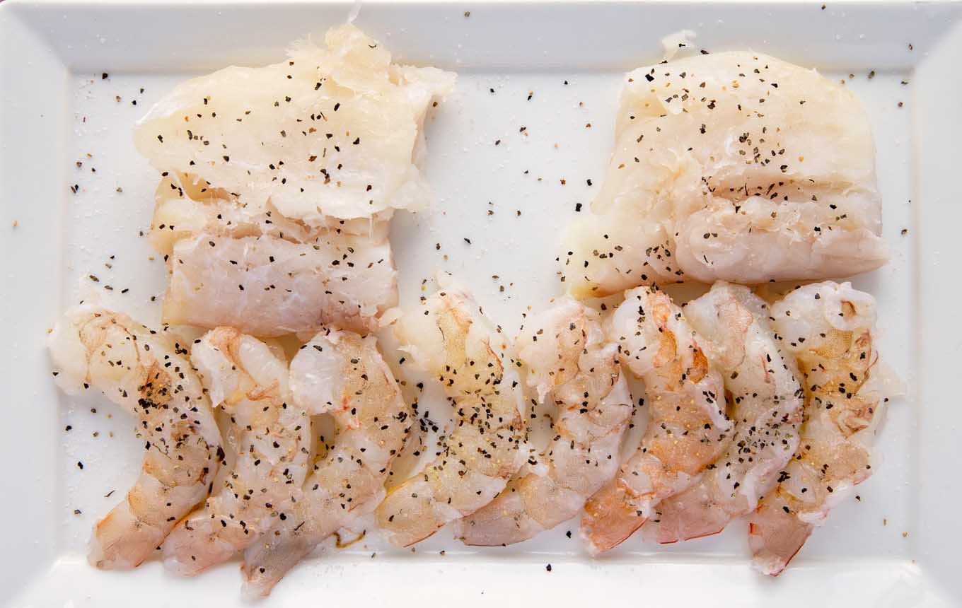 shrimp and cod seasoned with salt and pepper on a white platter