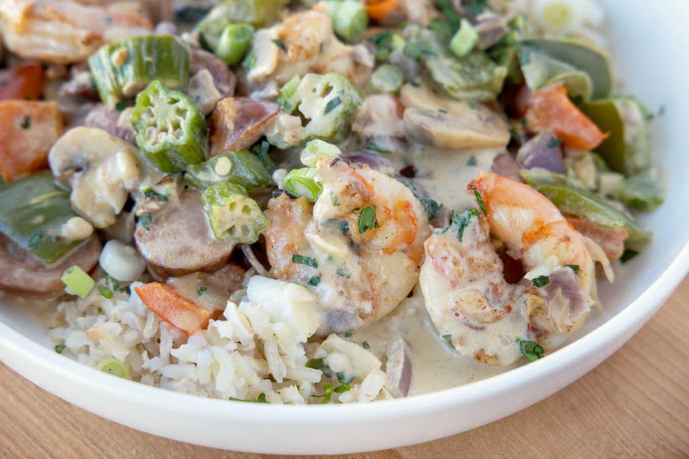 close up of shrimp and sausage over rice in a white bowl