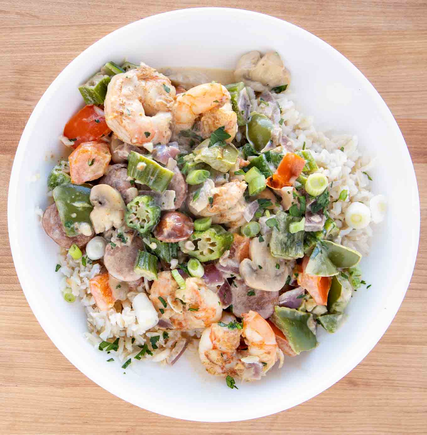 overhead shot of shrimp and sausage over rice in a white bowl