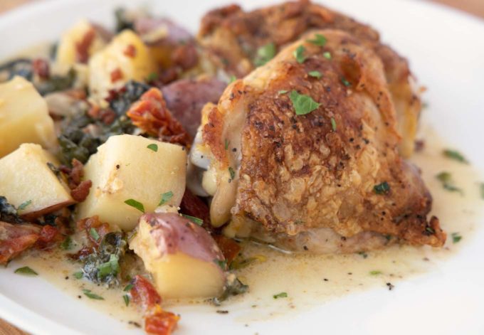 Tuscan Chicken with potatoes, baby kale and sun dried tomatoes on a white plate