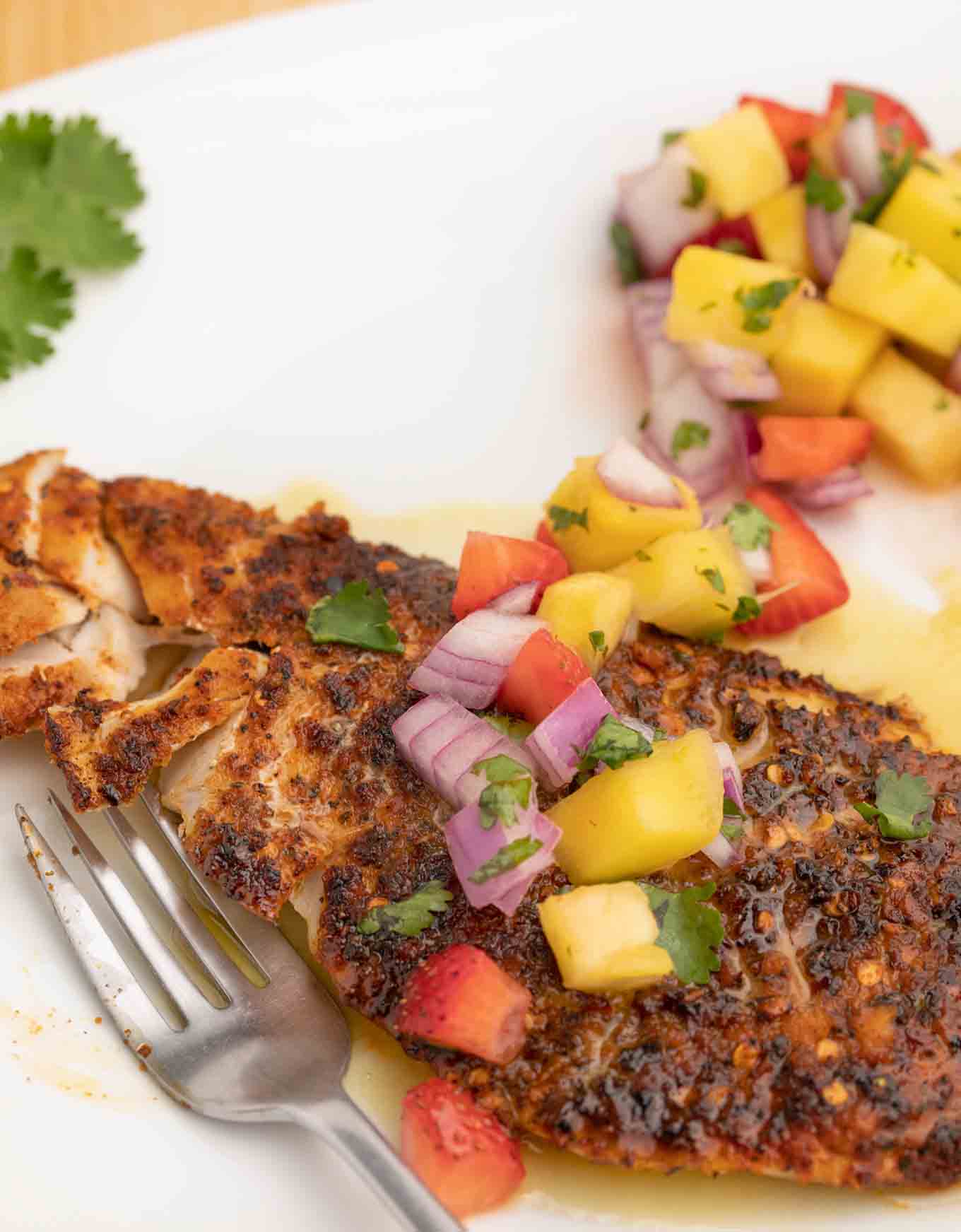 Blackened red snapper on a white plate with fruit salsa.