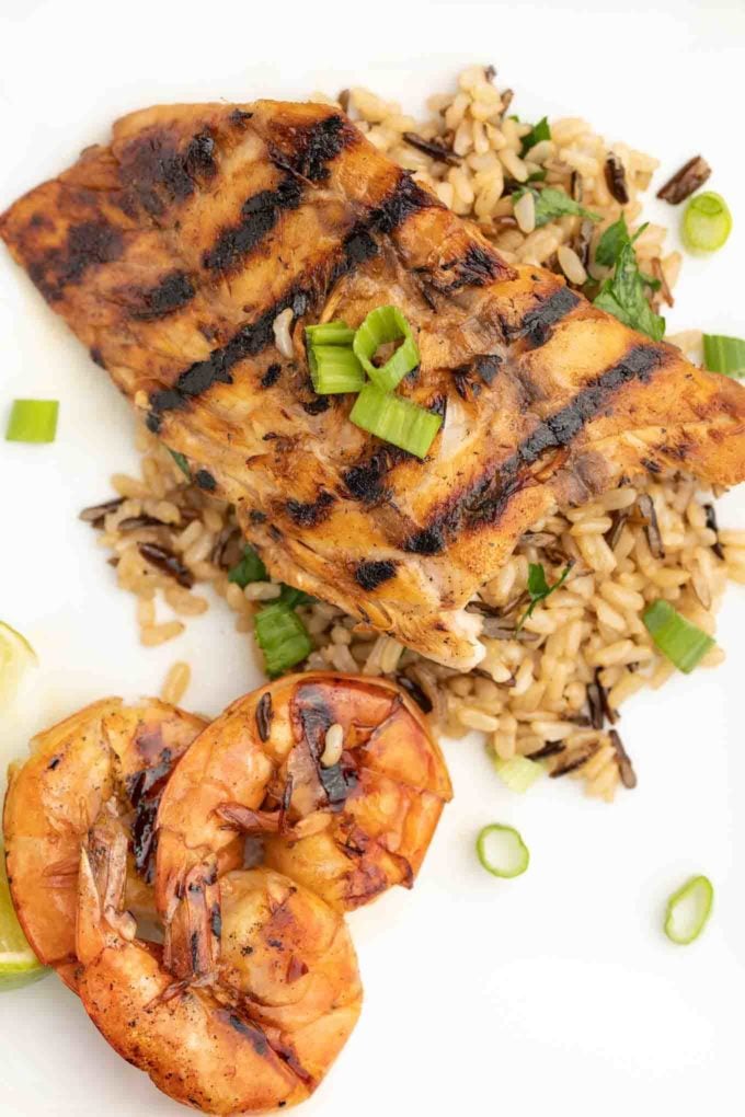 grilled rockfish on a bed of rice next to grilled shrimp on a white plate