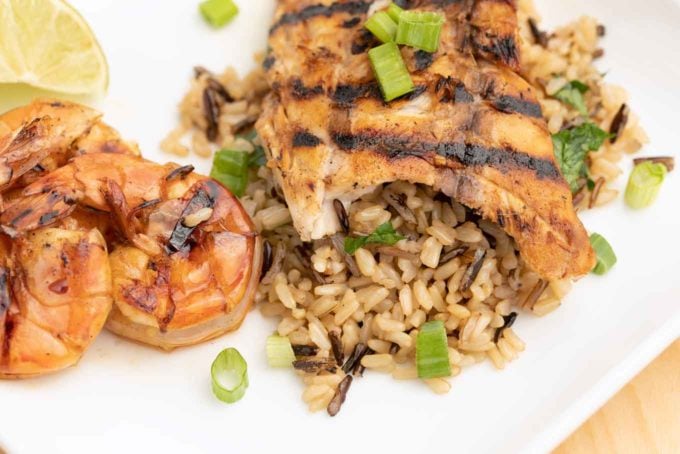 grilled rockfish on a bed of rice next to grilled shrimp on a white plate