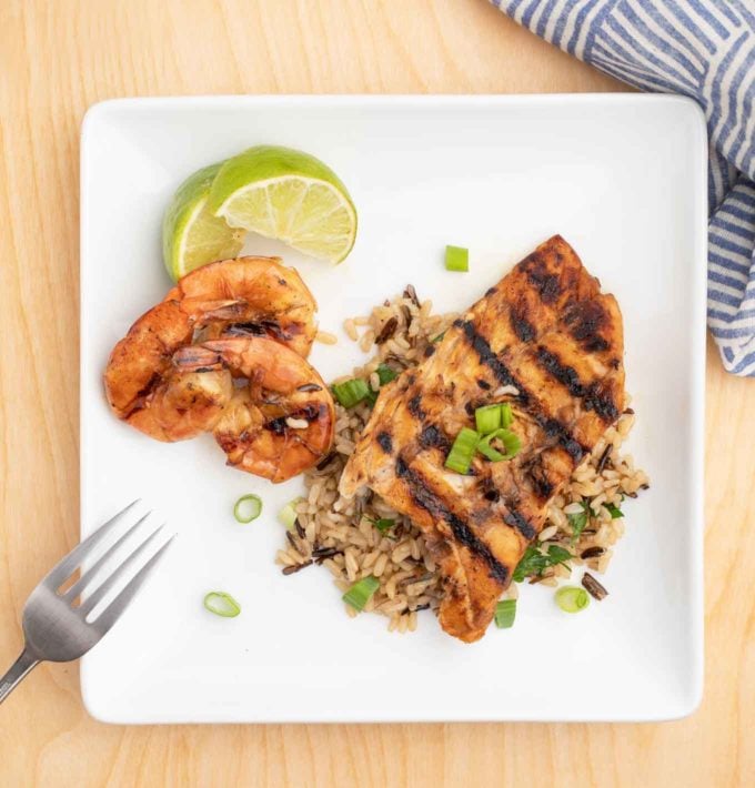 overhead view of grilled rockfish on a bed of rice next to grilled shrimp on a white plate