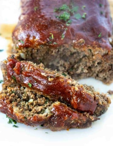 sliced meatloaf with the rest of meatloaf on a white platter