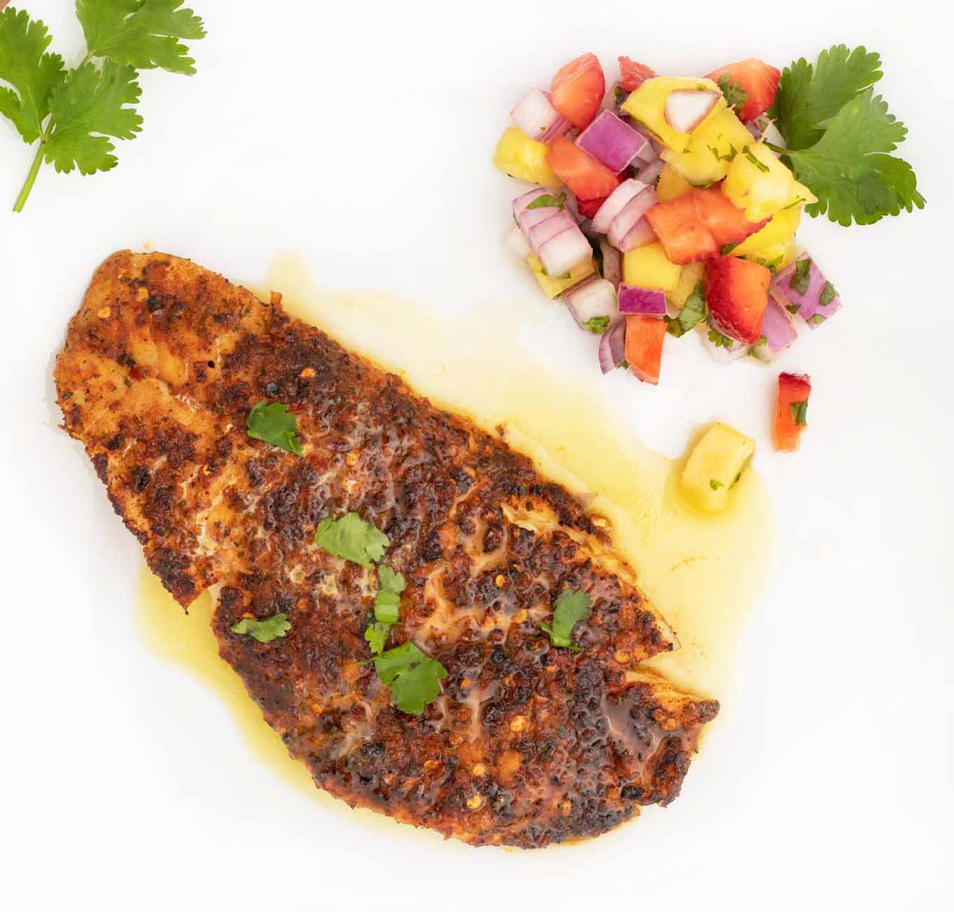 cooked cajun style florida snapper fillet with fruit salsa and lime margarita sauce on a white plate