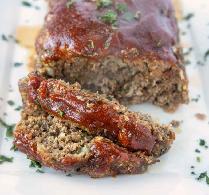 two slices of meatloaf in front of the rest of the meatloaf on a white platter.