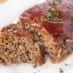 two slices of meatloaf in front of the rest of the meatloaf on a white platter