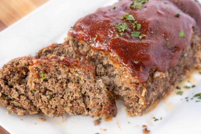 two slices of meatloaf in front of the rest of the meatloaf on a white platter