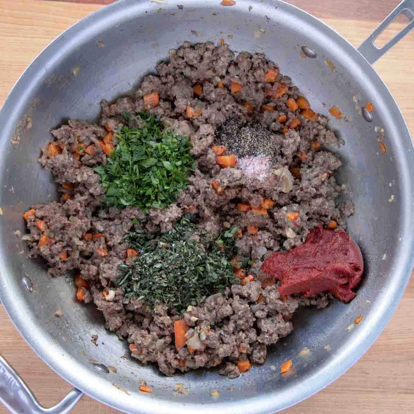 Cooked ground beef in large skillet with seasonings, herbs and tomato paste added to pan.