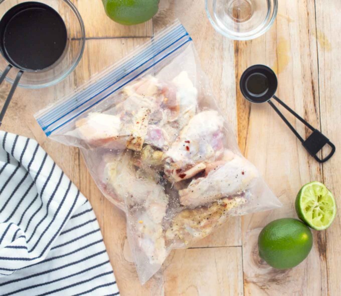 chicken wings in a ziplock bag maninating next to measuring cups and lime halves