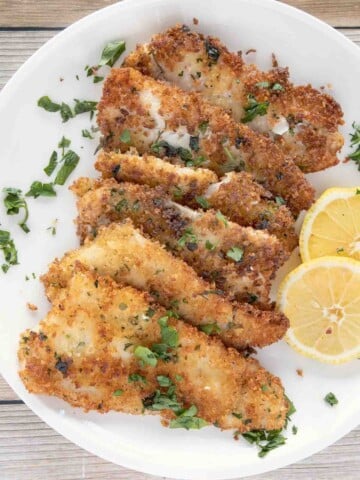 fried flounder filets on a white plate with lemon circles