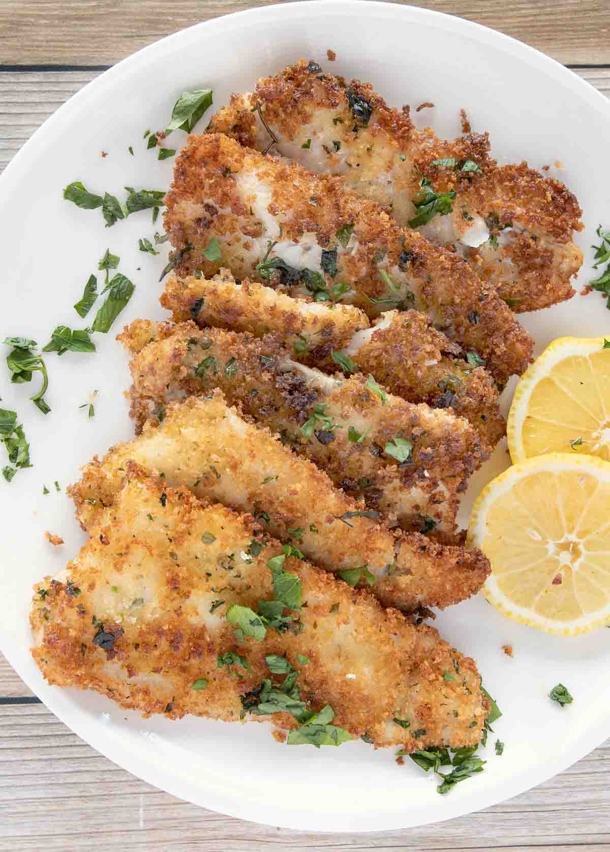 fried flounder filets on a white plate with lemon circles