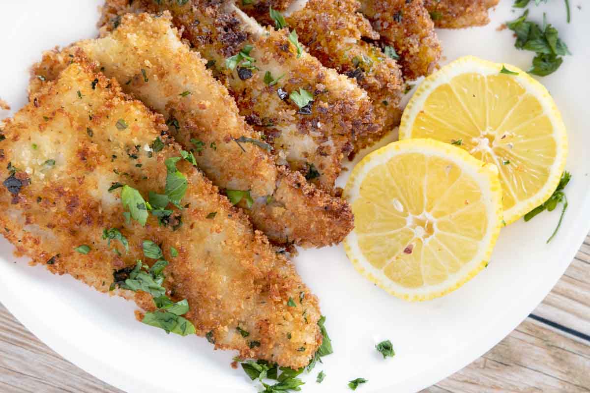 fried flounder filets on a white plate with lemon circles