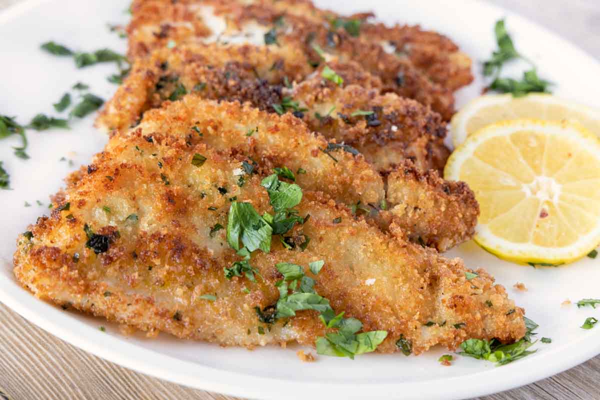 fried flounder filets on a white plate with lemon circles