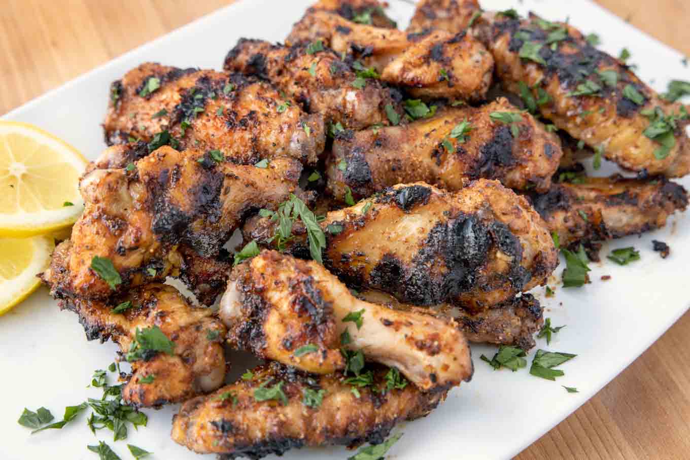 stack of grilled dry rub lemon pepper chicken wings on a white platter