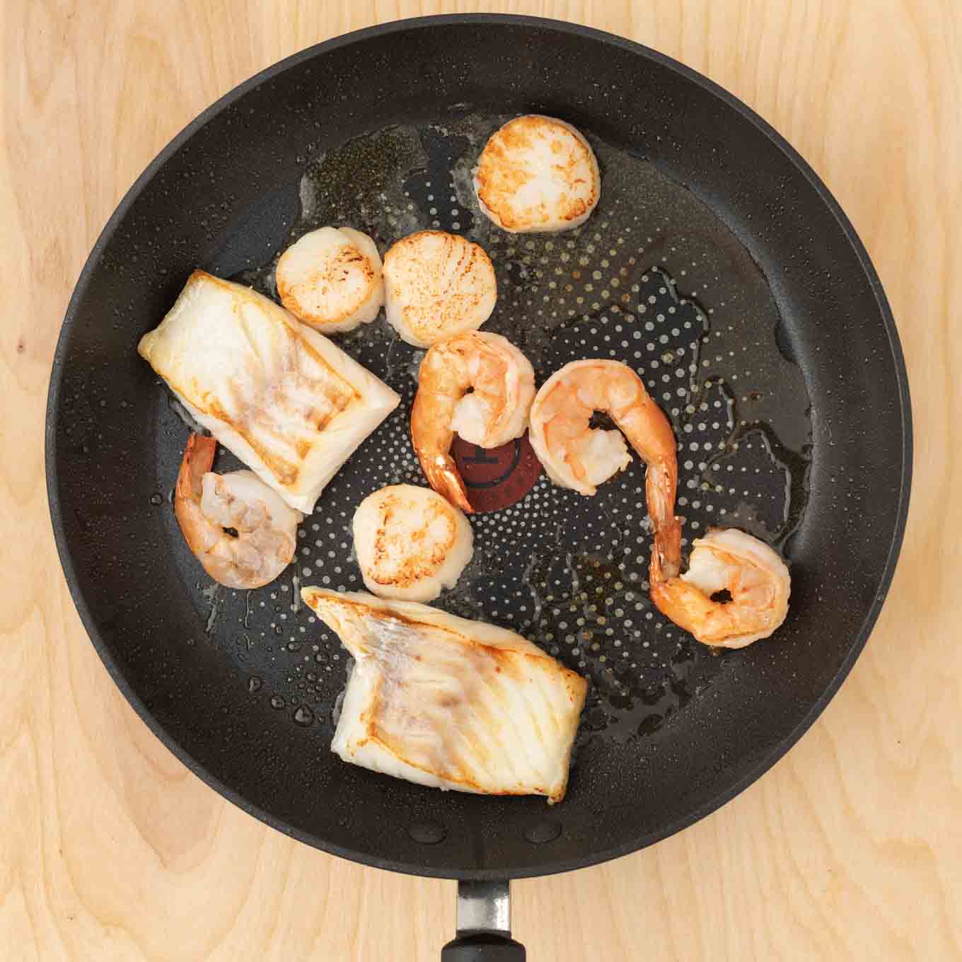 fish, shrimp and scallops in a pan cooking