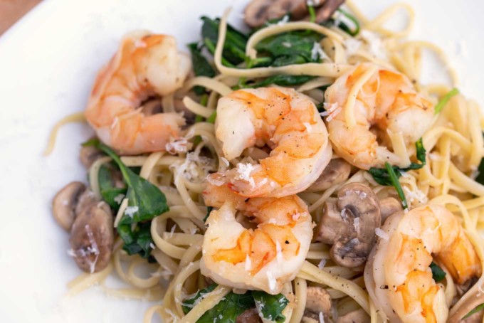 garlic shrimp with mushrooms and spinach served over linguine on a white plate