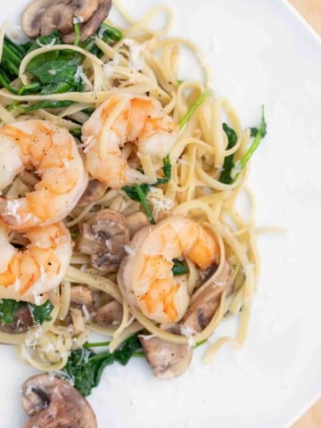 garlic shrimp with mushrooms and spinach served over linguine on a white plate