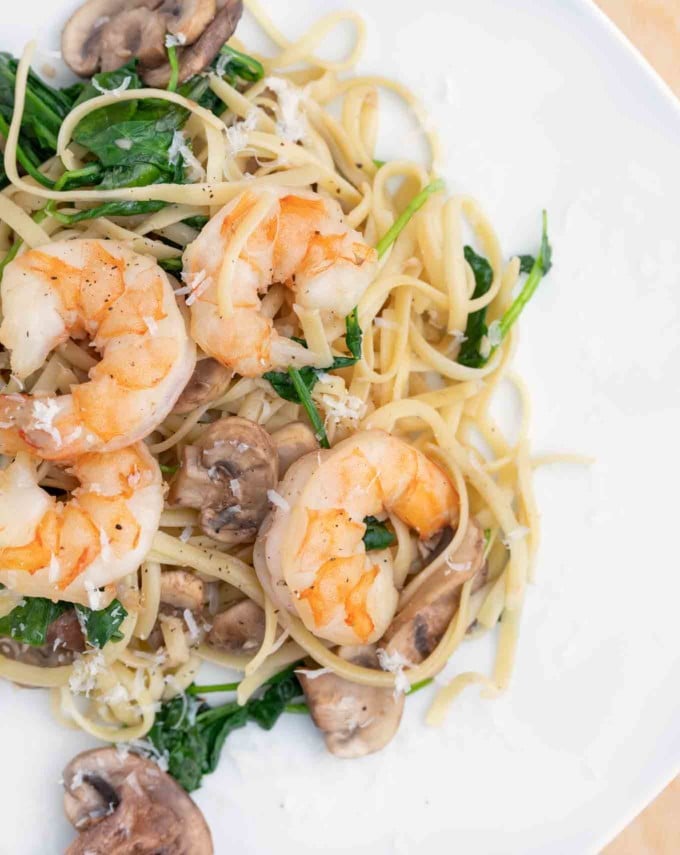 garlic shrimp with mushrooms and spinach served over linguine on a white plate