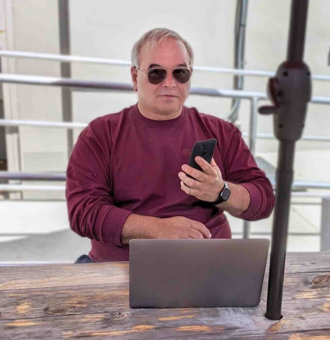 Chef Dennis on his phone and laptop sitting at a picnic table