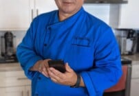 chef dennis in his kitchen holding a phone and smiling