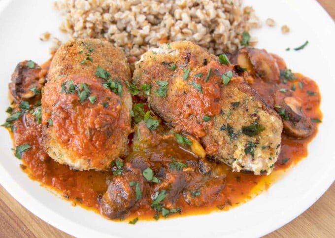 two beef braciole with mushroom tomato sauce and farro on a white plate